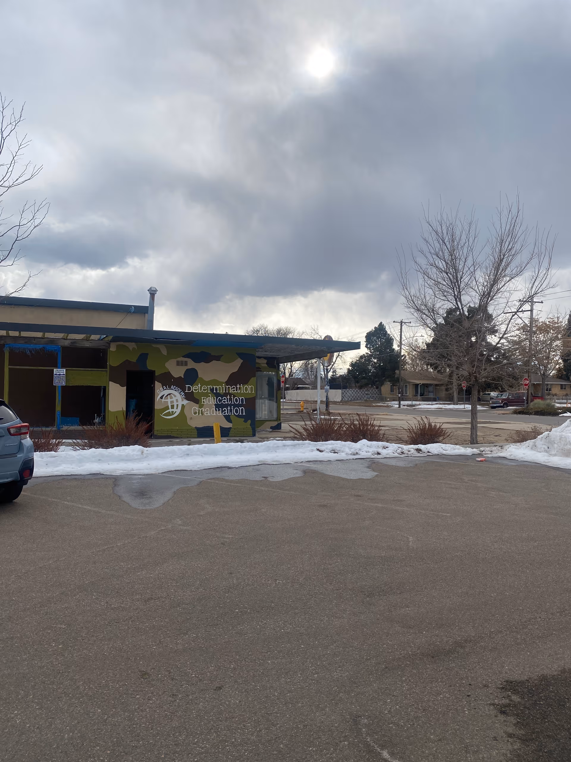 Exterior view of a building with a colorful mural, parked cars, and snow on the ground.