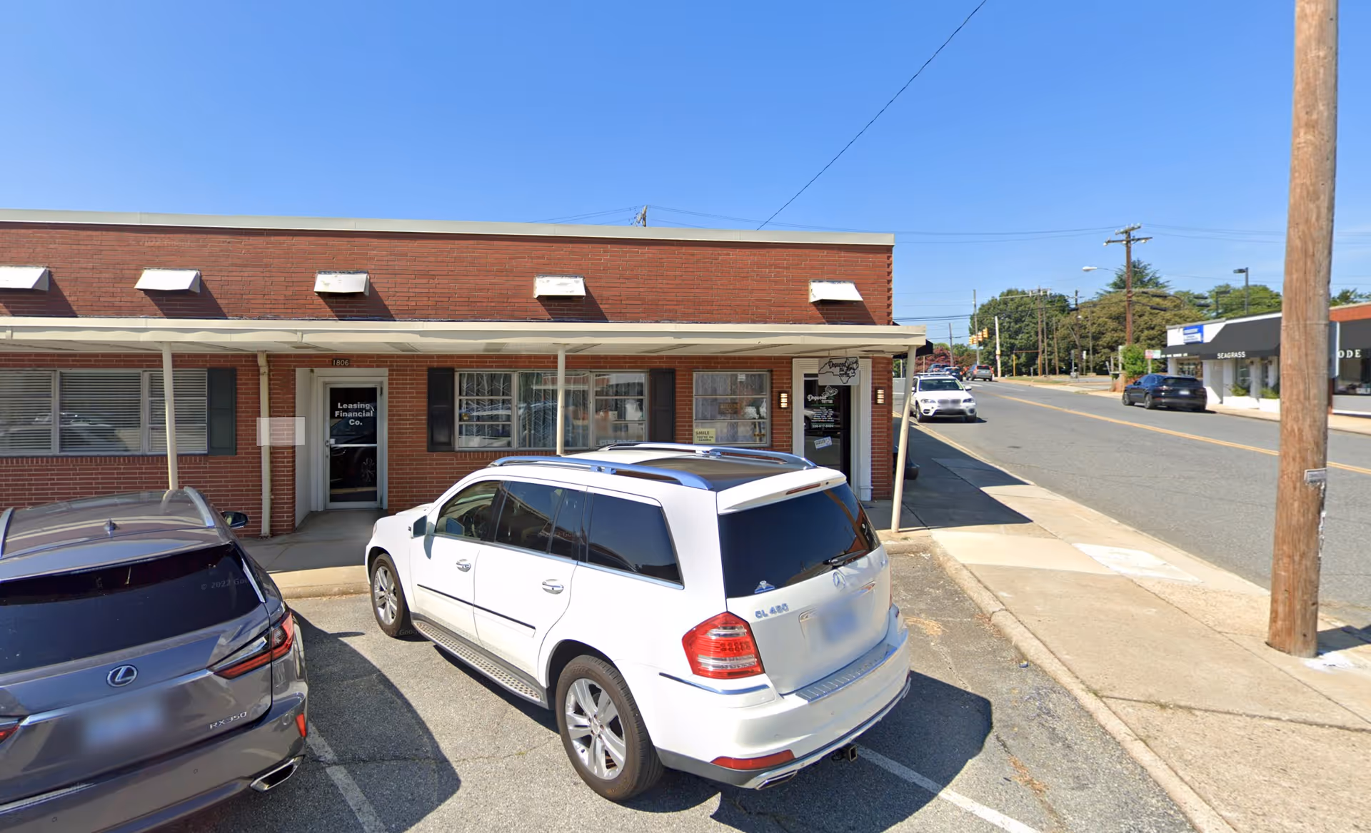 Brick storefront building with awnings, parked cars, and a sidewalk along the street.