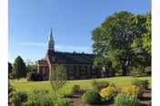 Exterior of Christ's Home Retirement Community Shepherds Crossing building with a steeple, lawn, and trees.