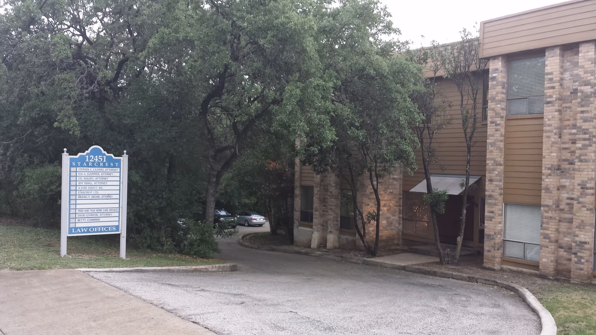 Brick building exterior with a driveway, trees, and a law offices sign on the left.