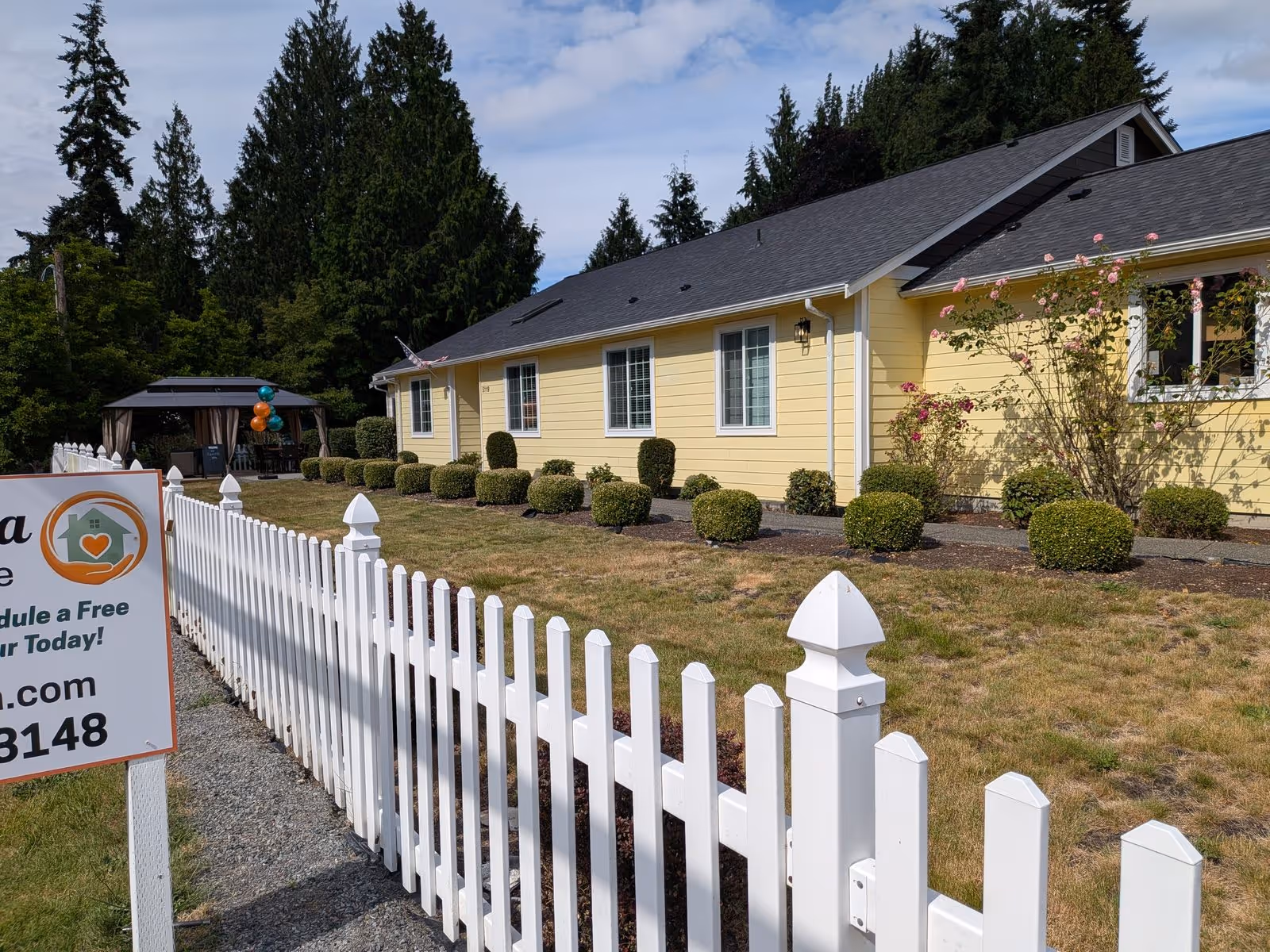 Yellow Edmonds Villa Adult Family Home exterior with white picket fence and landscaped shrubs.