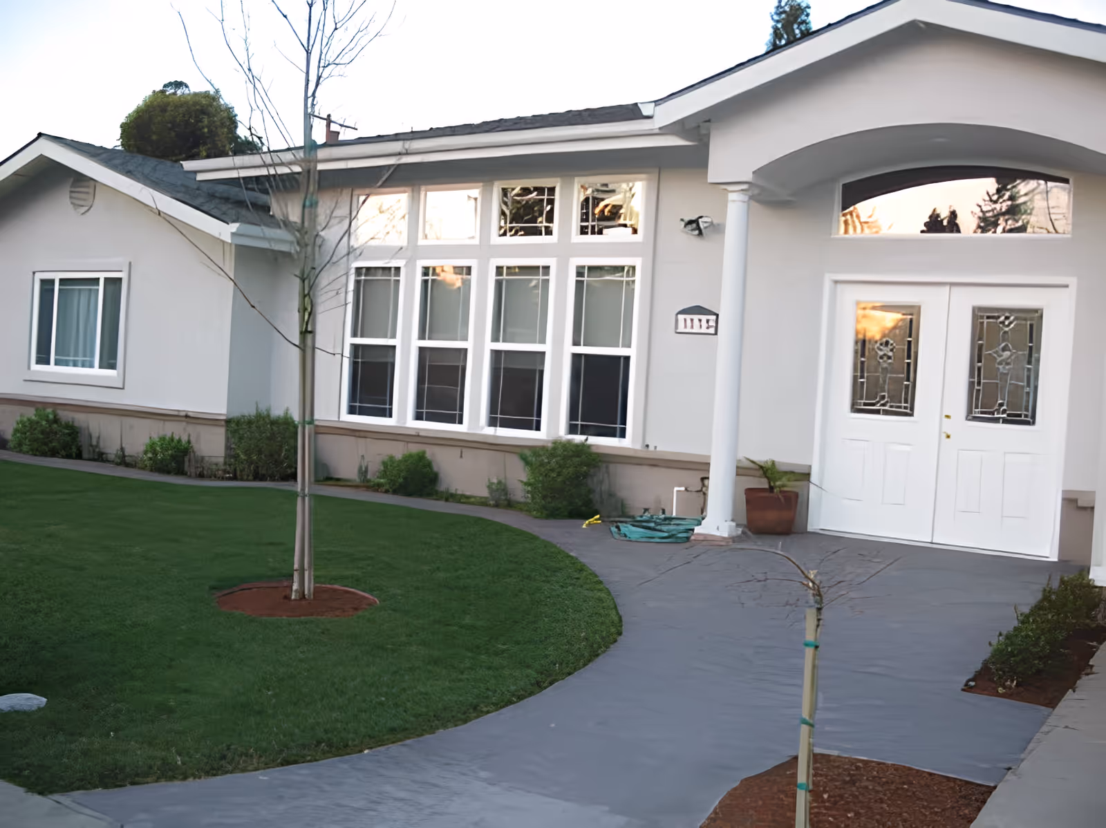 Front exterior of a single-story home with a curved walkway, lawn, and double glass-paneled entrance doors.