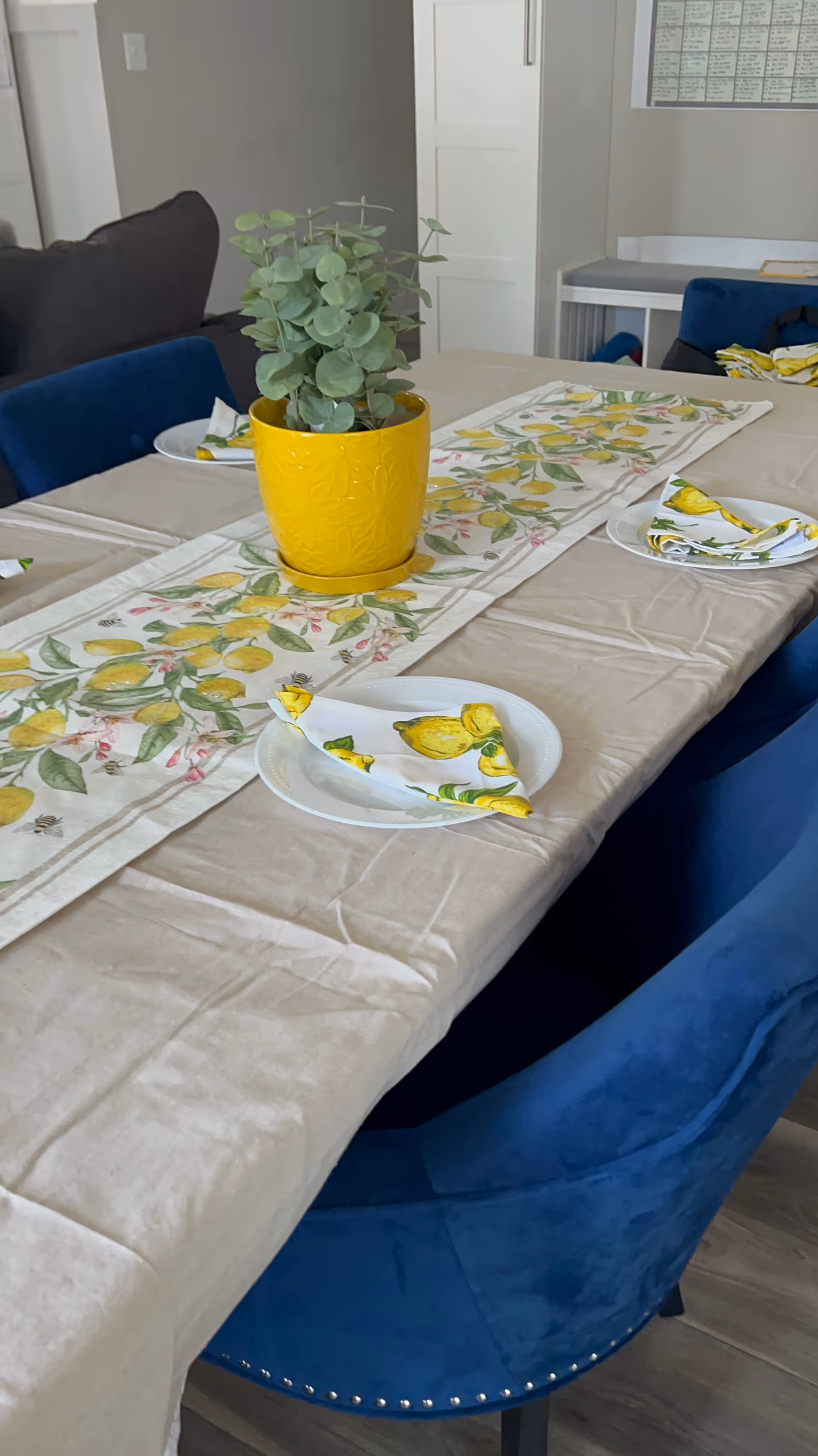 In a dining room, a long table with lemon decor and blue chairs.