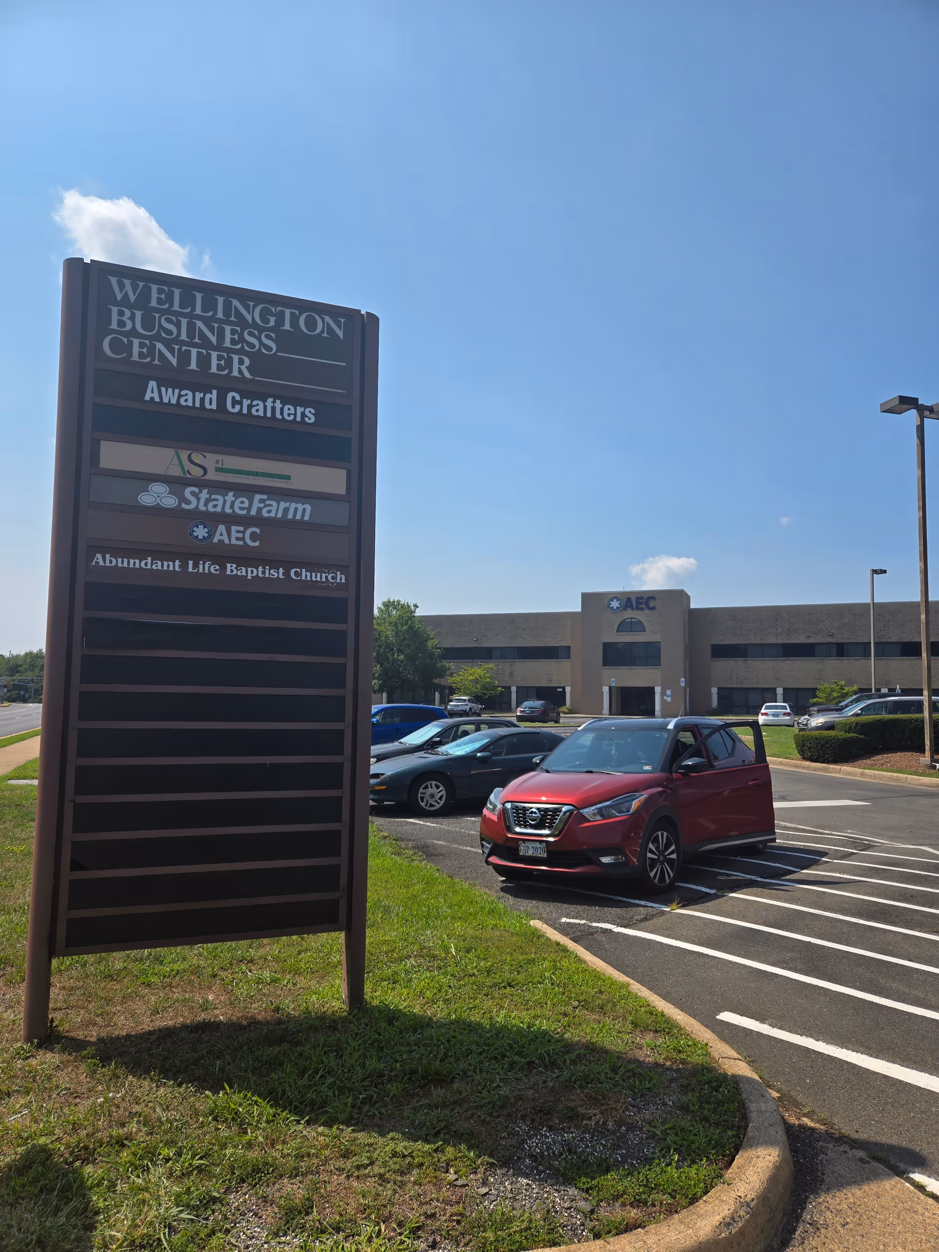 Tall sign for Wellington Business Center beside a parking lot with a front-facing building.