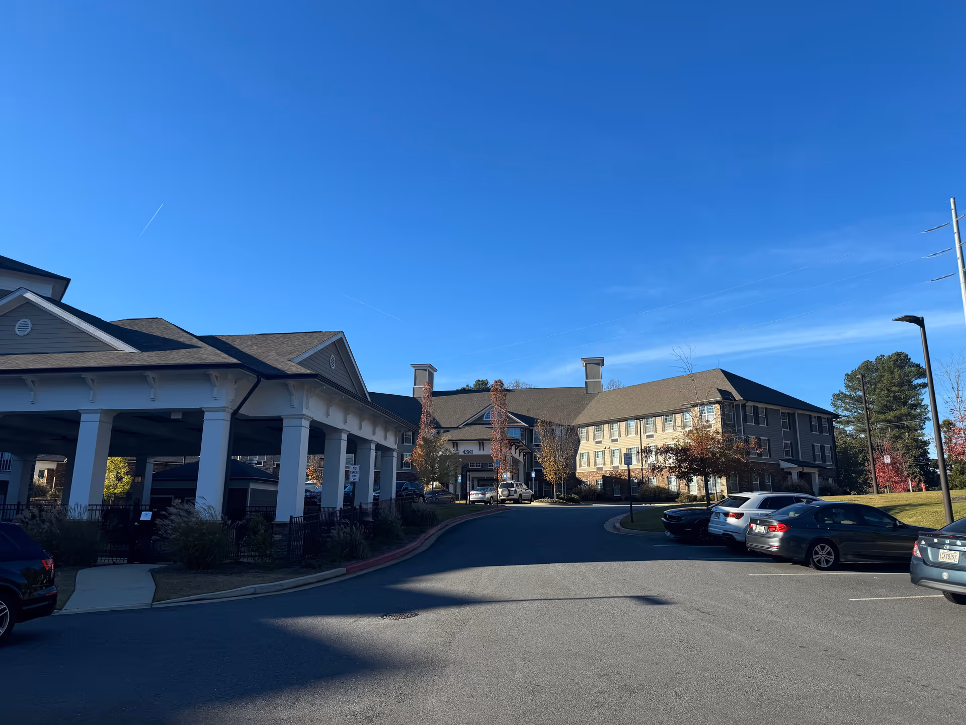 A senior living campus exterior with a covered entrance and parked cars under a blue sky.