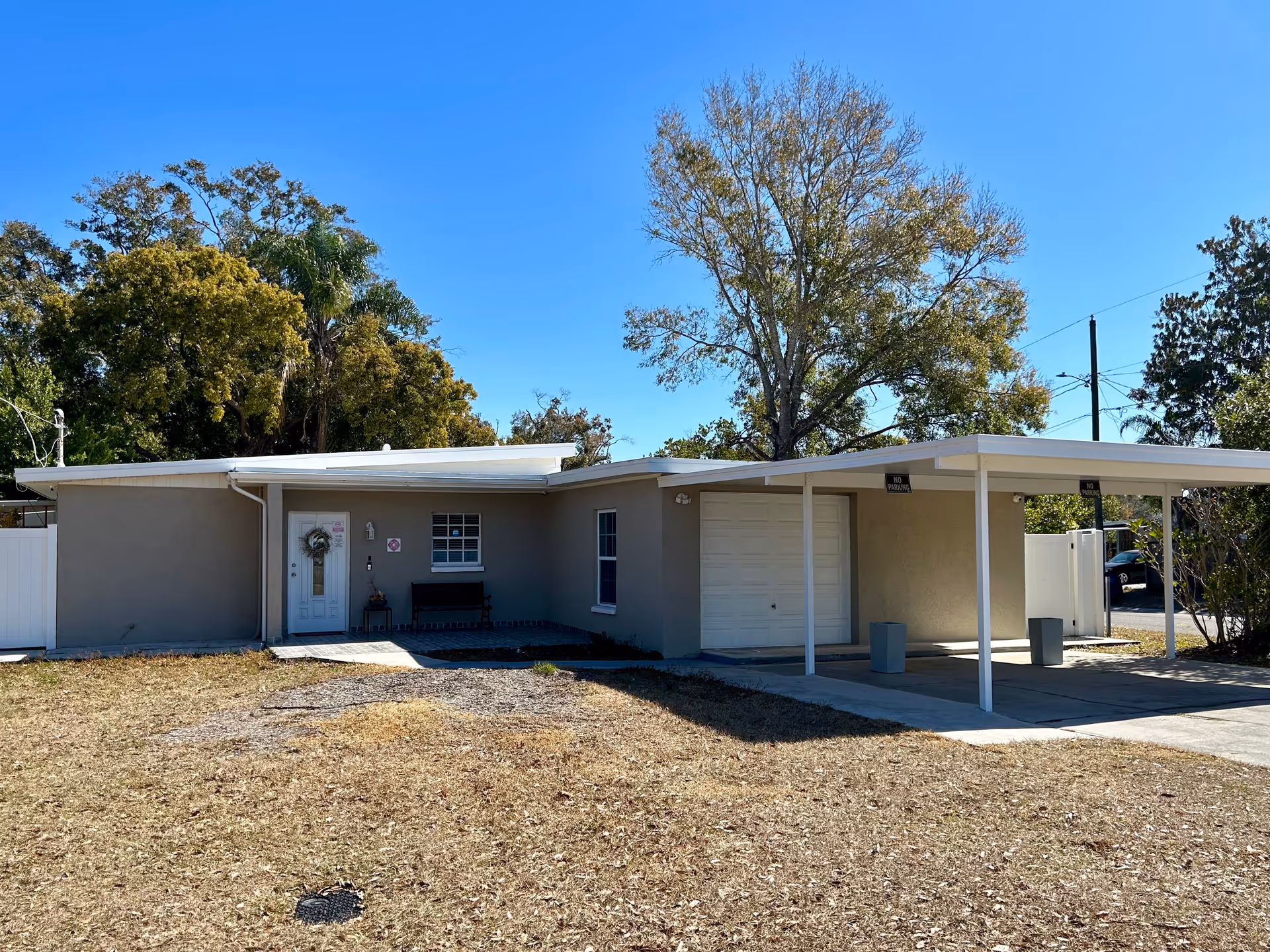 Single-story gray facility with a covered carport and front entrance under a clear blue sky.
