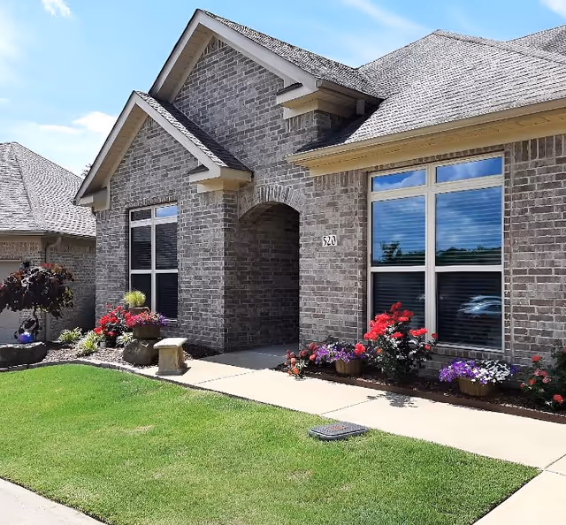 Brick senior living facility entrance with arched doorway and flower planters.