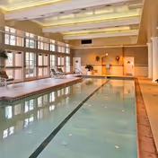Indoor pool area at a senior living facility with large windows and lounge chairs.