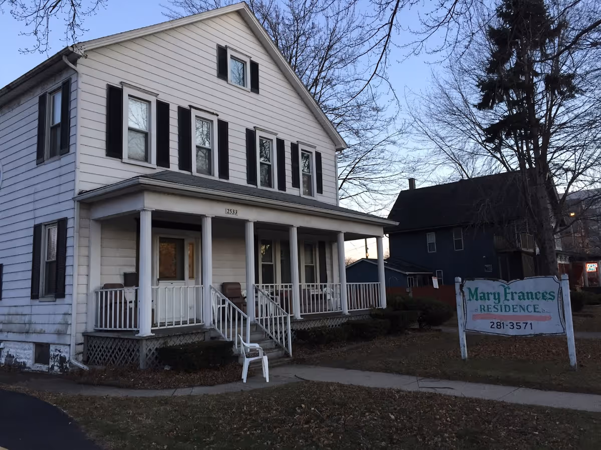 Two-story white house with a front porch and a yard sign reading 'Mary Frances Residence'.