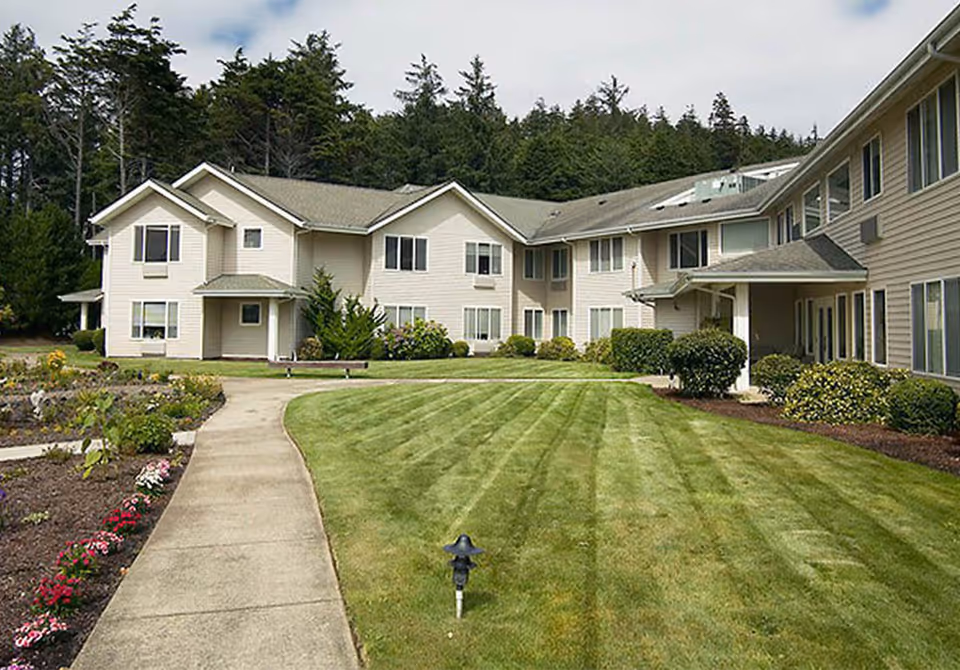 Exterior view of a senior living facility with beige buildings, green lawn, and landscaped walkways.