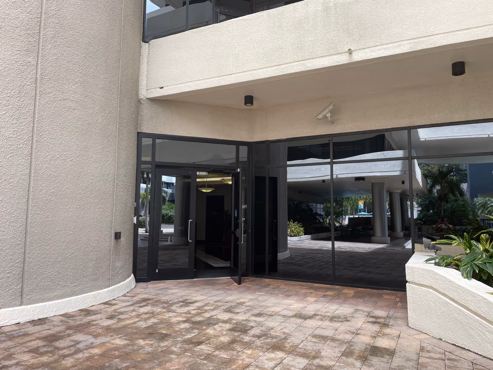 Exterior view of a building entrance with glass doors, beige walls, and a tiled walkway.