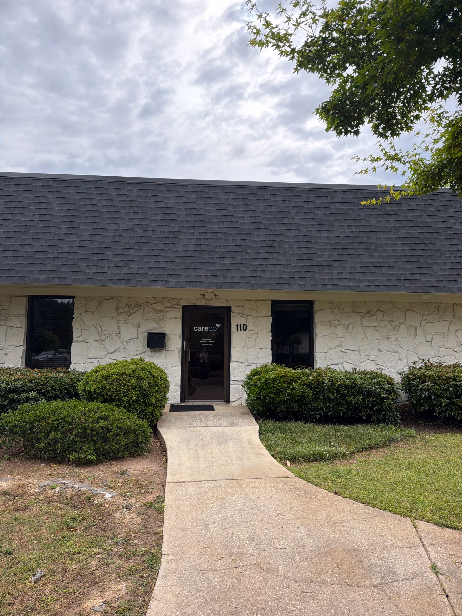 Front view of CareCo entrance with stone facade, concrete path, and shrubs.