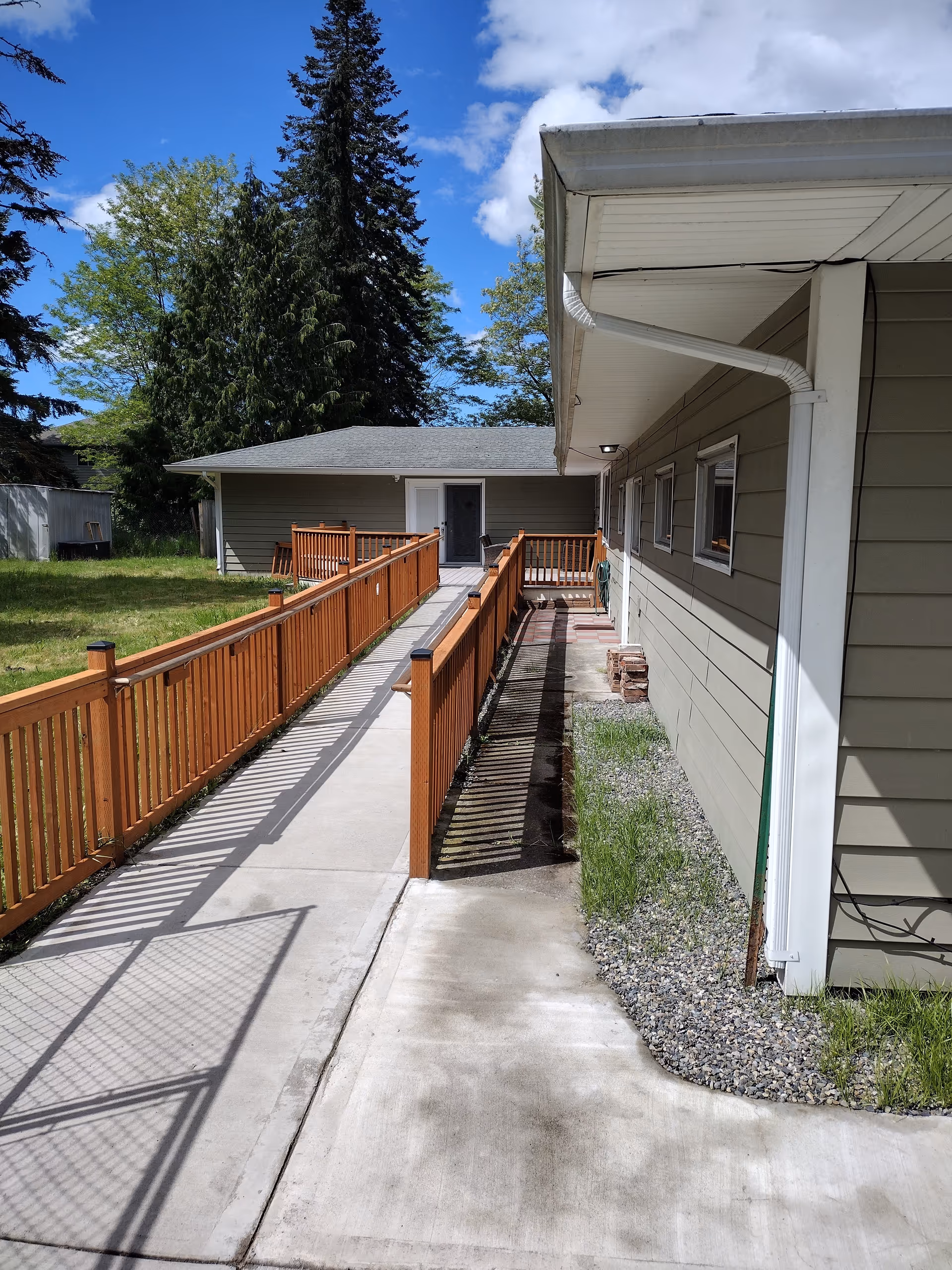 Exterior walkway and ramp beside a beige building with wooden railing.