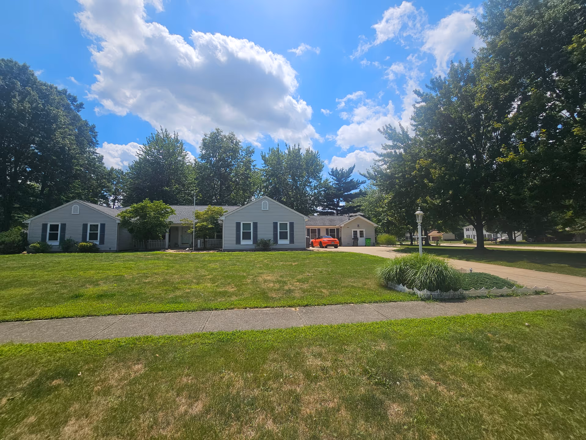 Single-story light-gray building complex with manicured lawn, trees, and a red car in the driveway.