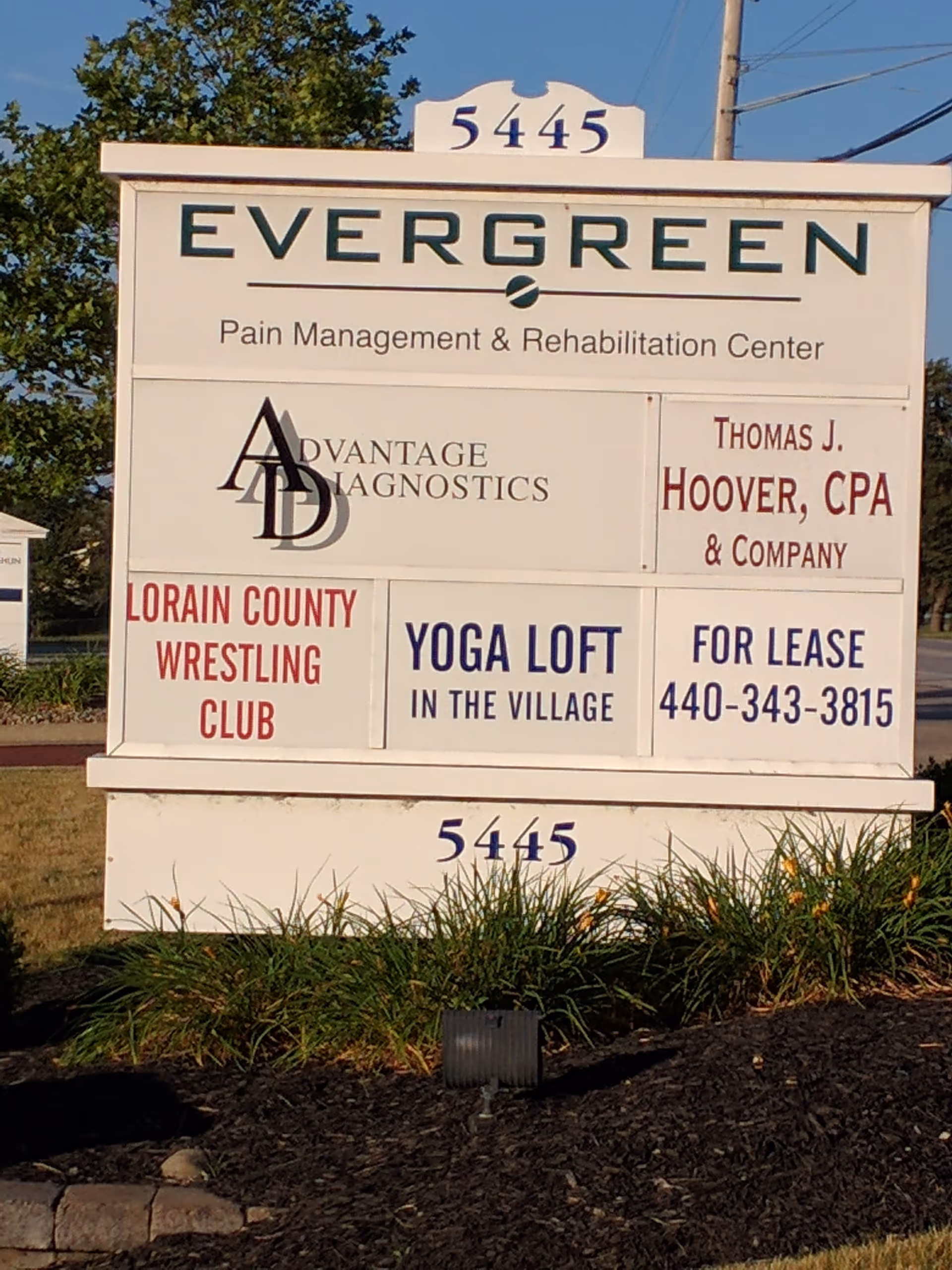 Outdoor signboard shows Evergreen Pain Management & Rehabilitation Center with multiple ads.