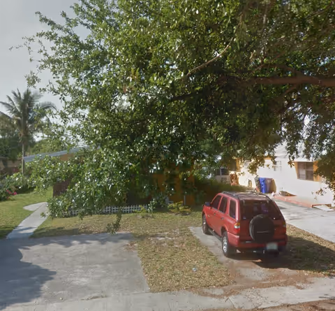 Red SUV parked beside a building with a large tree overhanging the driveway