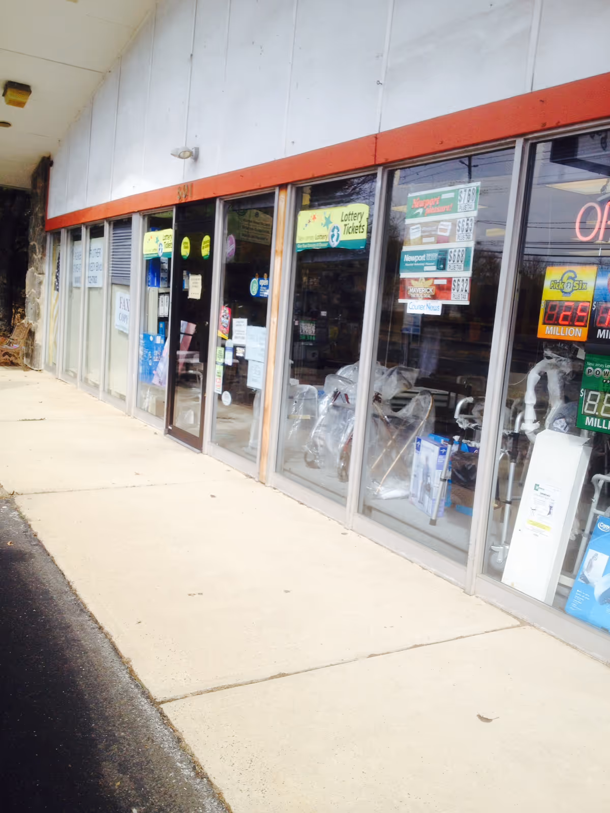 Exterior storefront with large glass windows displaying lottery signs and merchandise.