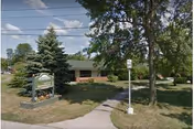 Front view of Clinton County Nursing Home with trees, lawn, and sign.
