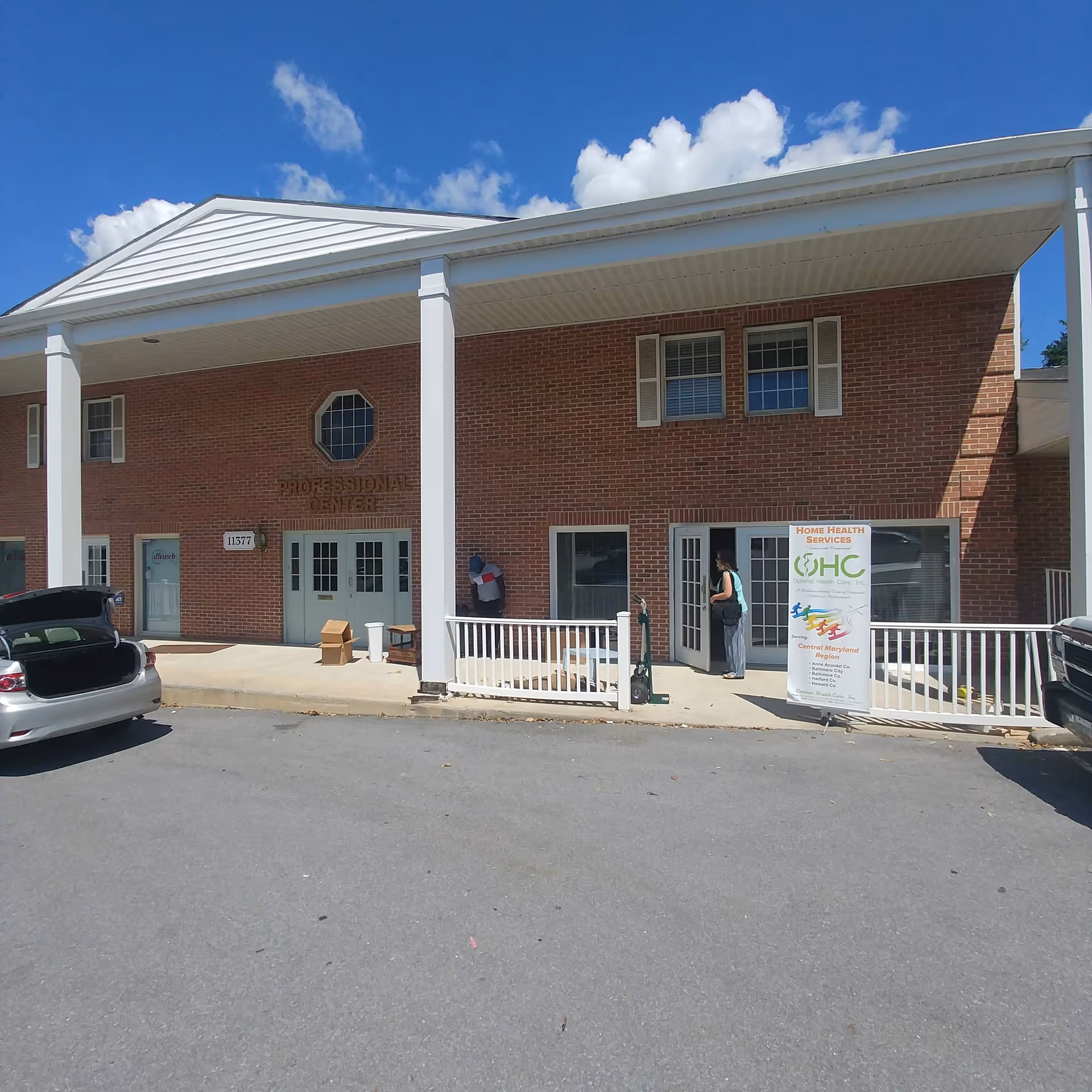Brick building with white columns and a covered entrance, banners and parked cars outside.