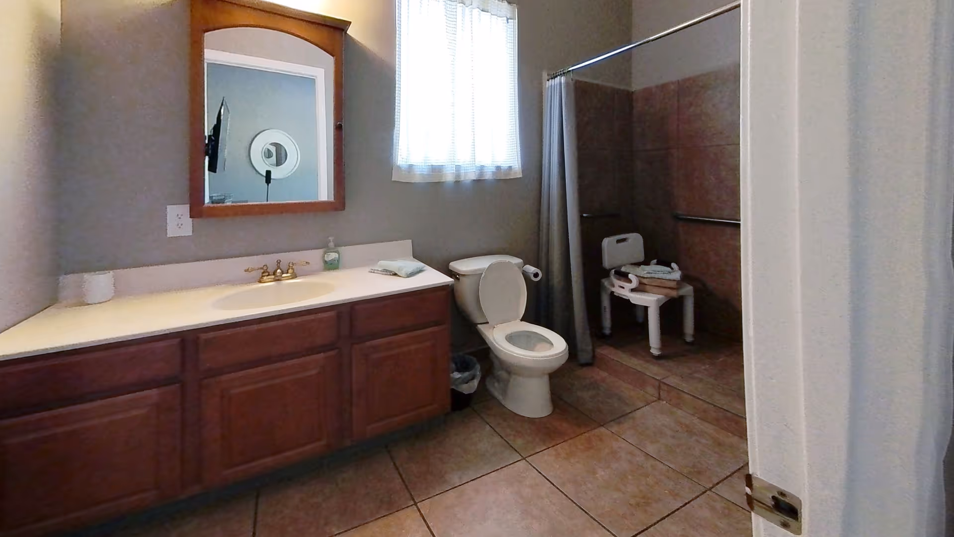 Bathroom in senior living facility with vanity, toilet, window, and shower chair.