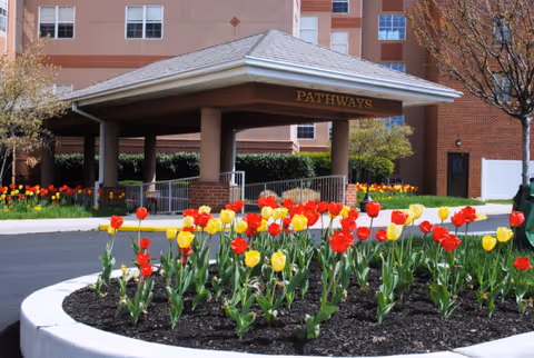 Front entrance porte-cochere with a 'PATHWAYS' sign and a bed of red and yellow tulips in the foreground.