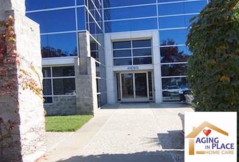 Modern glass-front building entrance with landscaped walkway and Aging in Place Home Care logo.