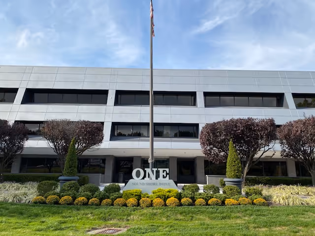 Front view of a modern office building with a flagpole and manicured landscaping.