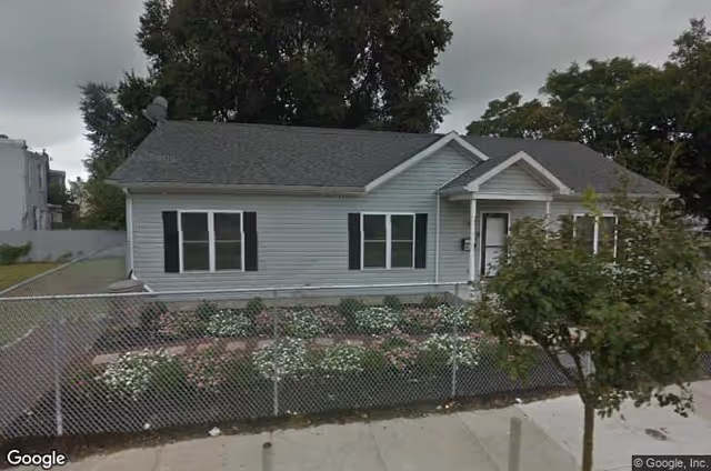 A single-story gray facility with a front yard, shrubs, and a chain-link fence.