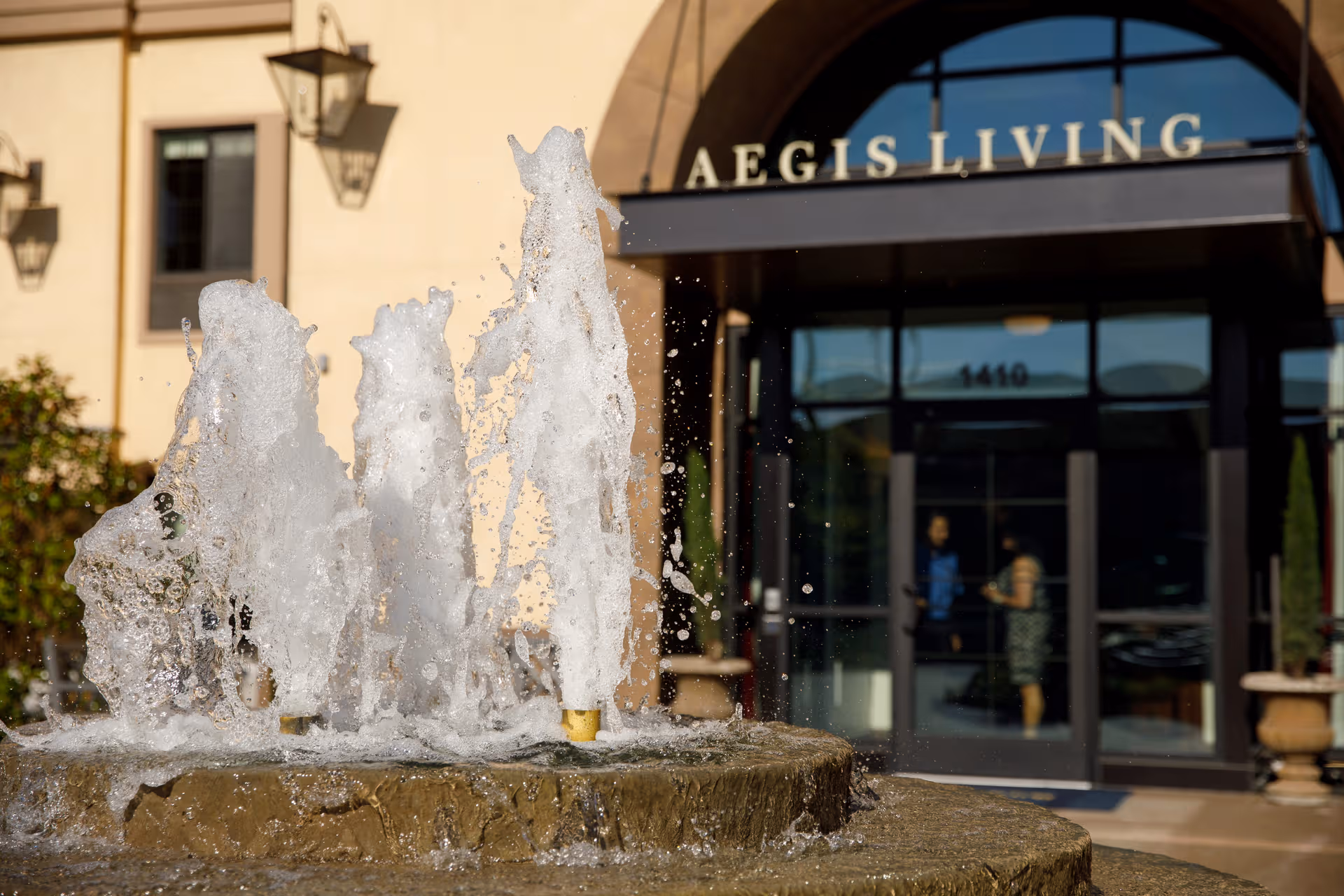 Front exterior of Aegis Living Ravenna with a fountain and glass entrance.