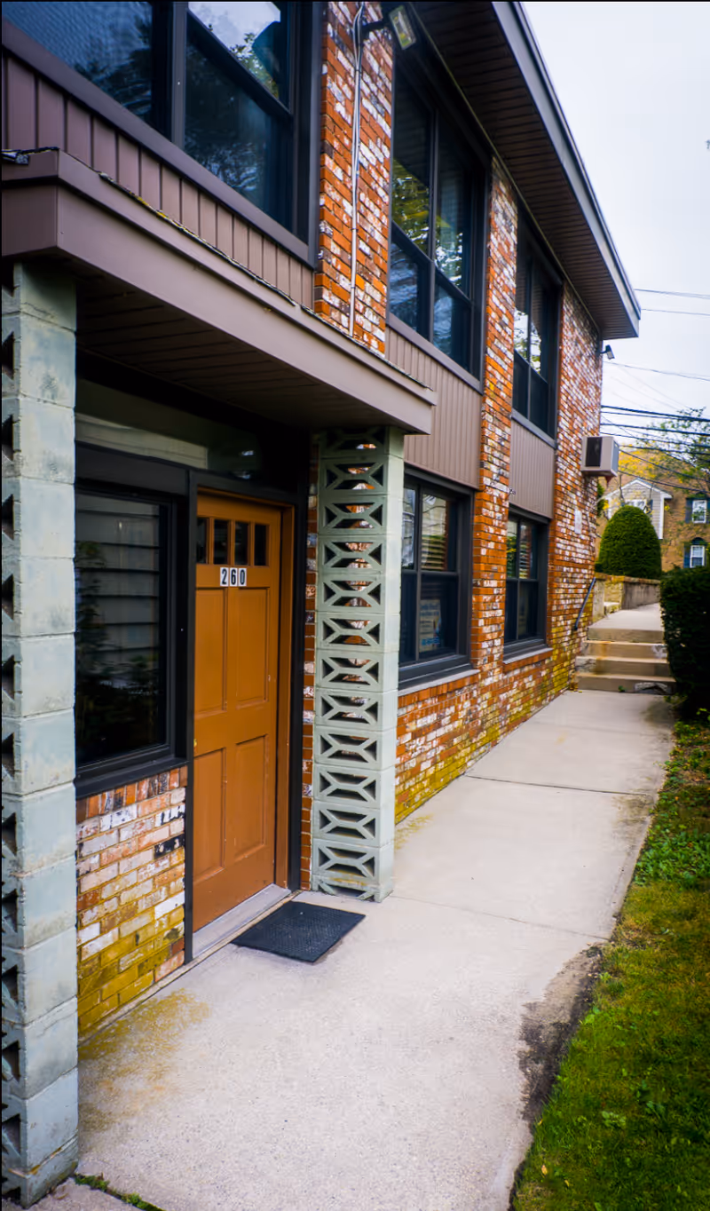 Exterior view of a brick senior home entrance with a wooden door and sidewalk.
