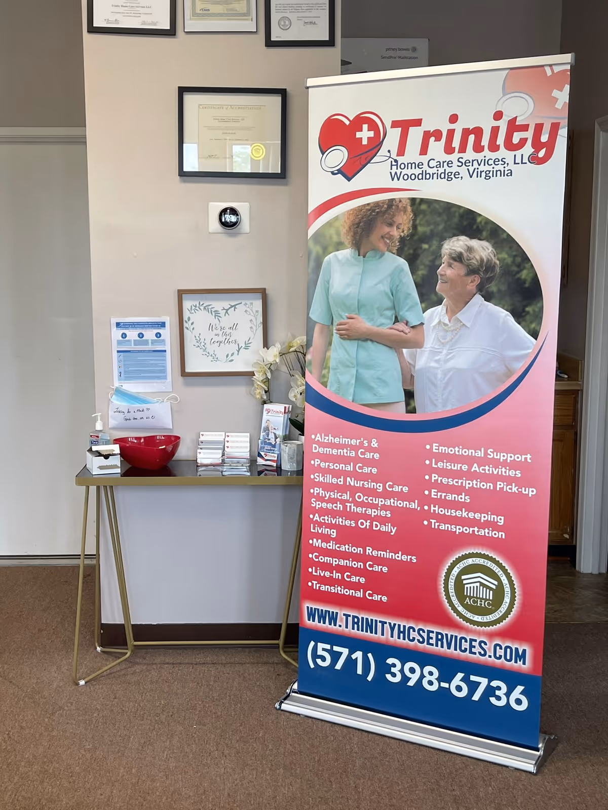 Indoor lobby with Trinity Home Care Services banner beside framed certificates on the wall.
