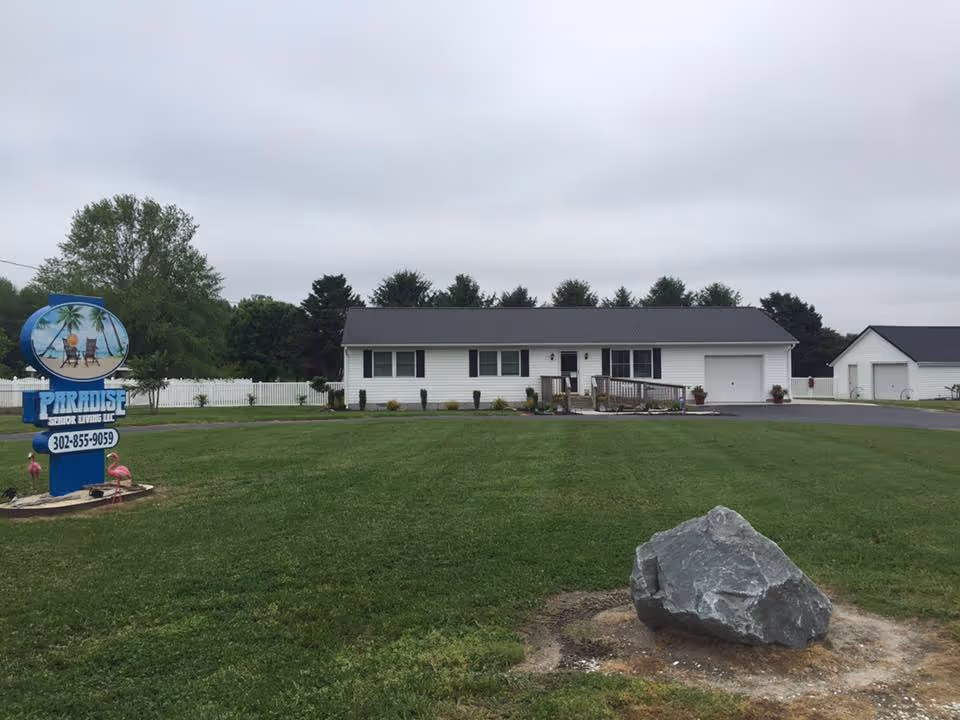 Single-story senior living facility with a manicured lawn, sign, and driveway in front