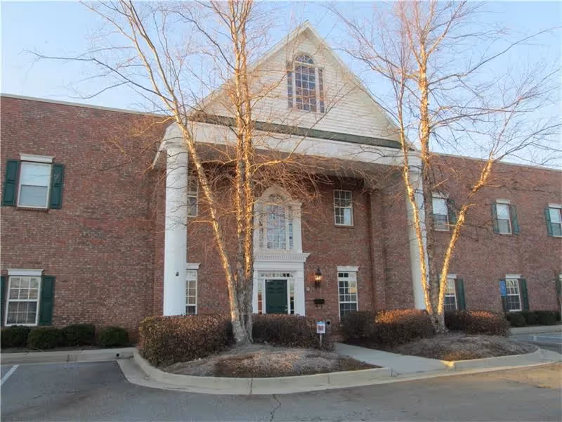 Brick senior living facility exterior with columns and leafless trees.