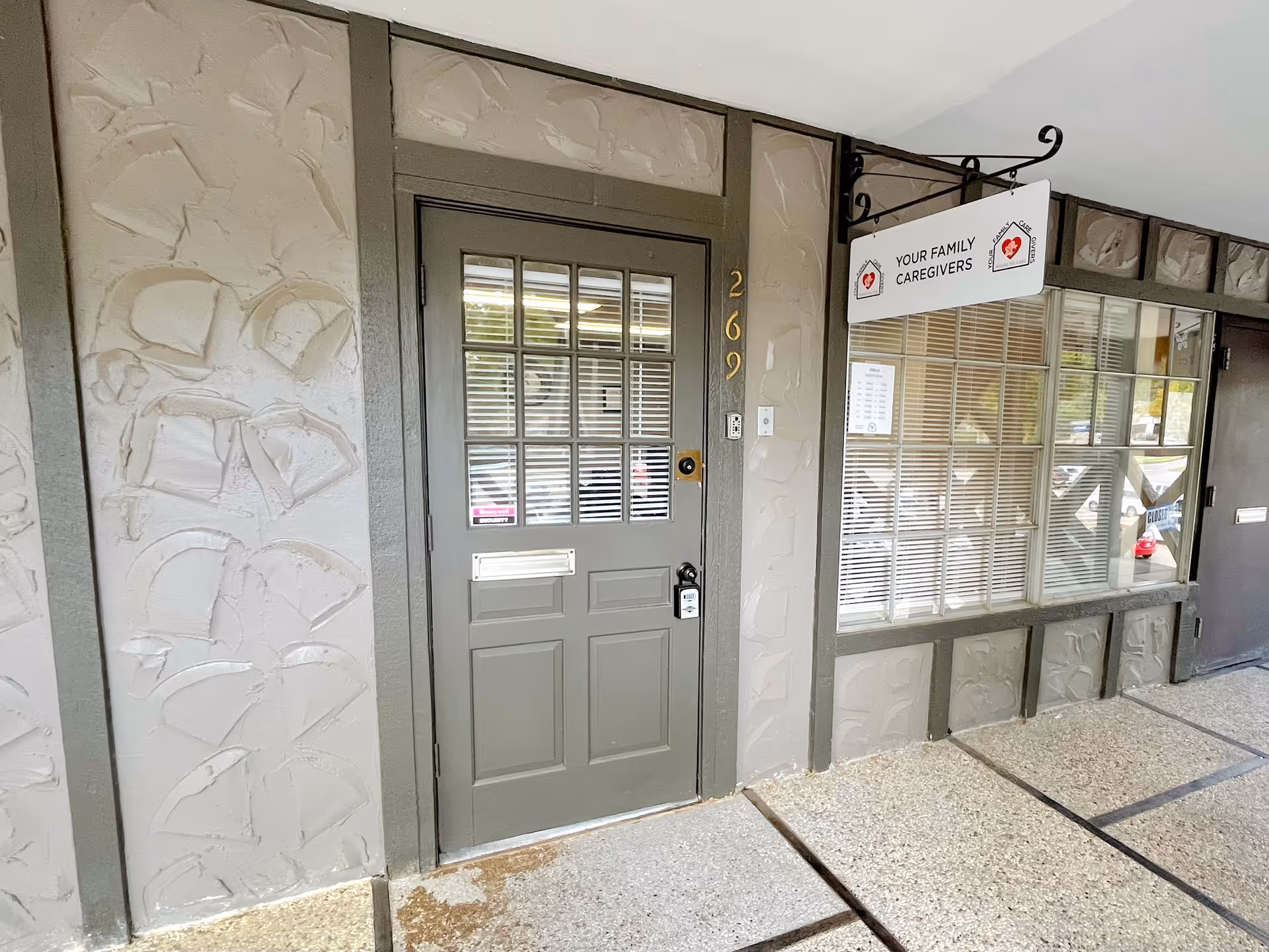 Front entrance of a senior care facility with a gray door and large windowed storefront.