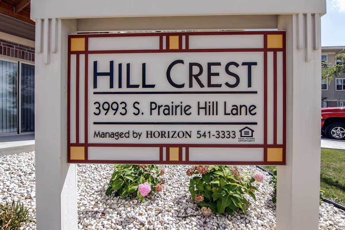 Exterior sign reads HILL CREST with address and a landscaped front yard.