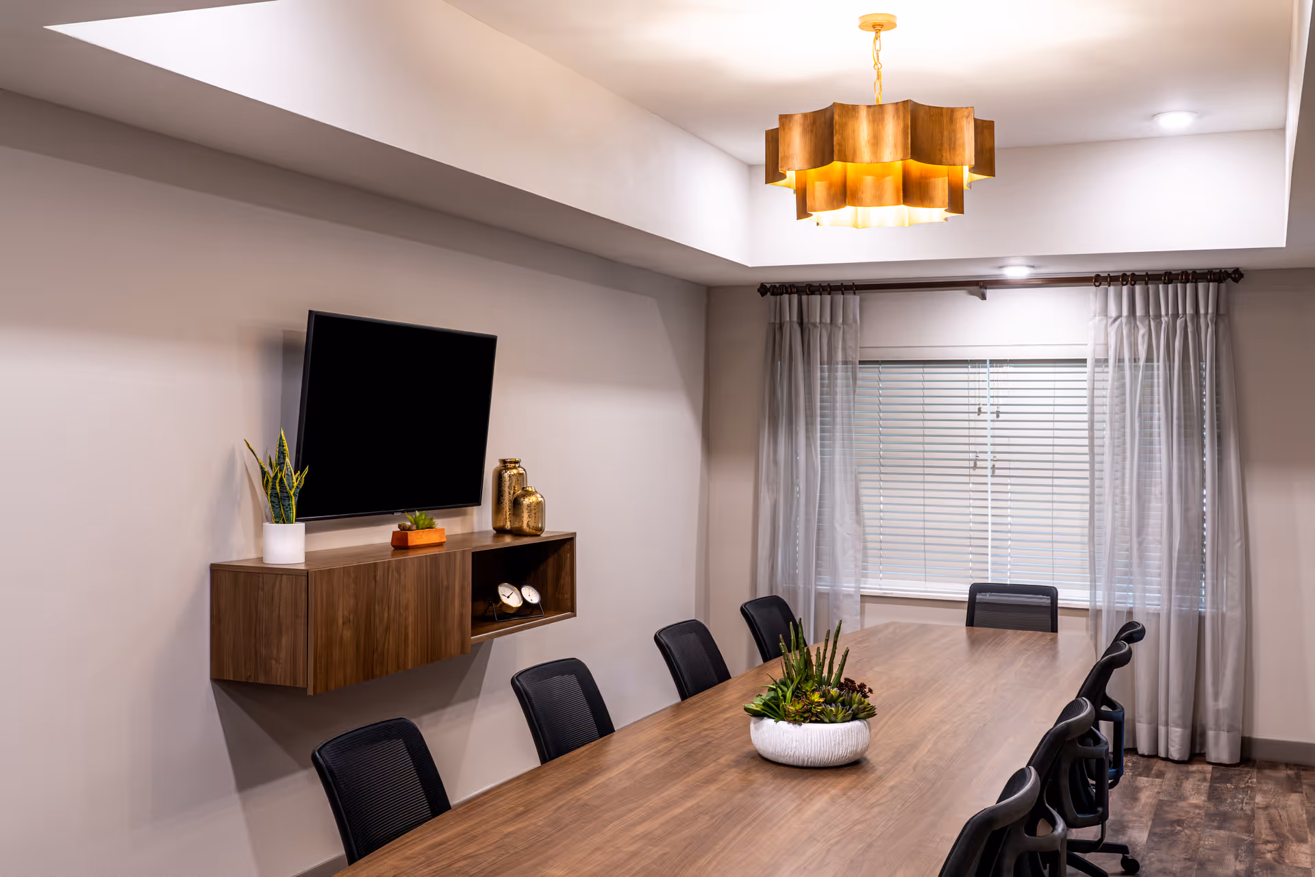 Modern conference room with a long wooden table, chairs, and a wall-mounted TV.