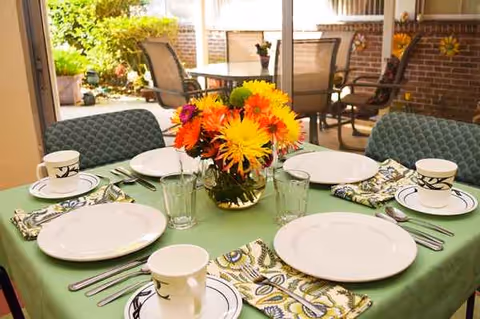 Outdoor dining patio visible through glass doors, with a neatly set table featuring a floral centerpiece.