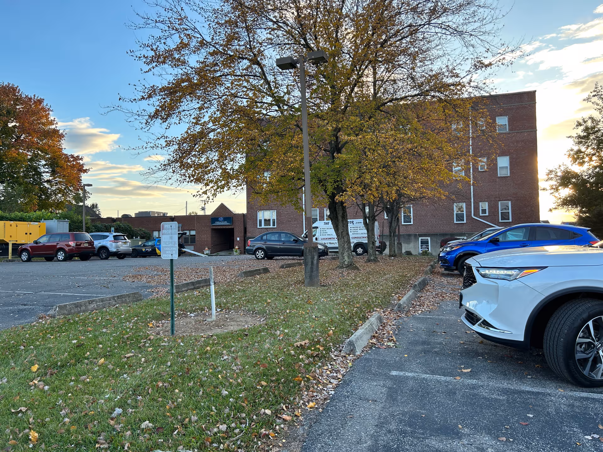 Exterior view of a brick building with parked cars and fall trees in front.