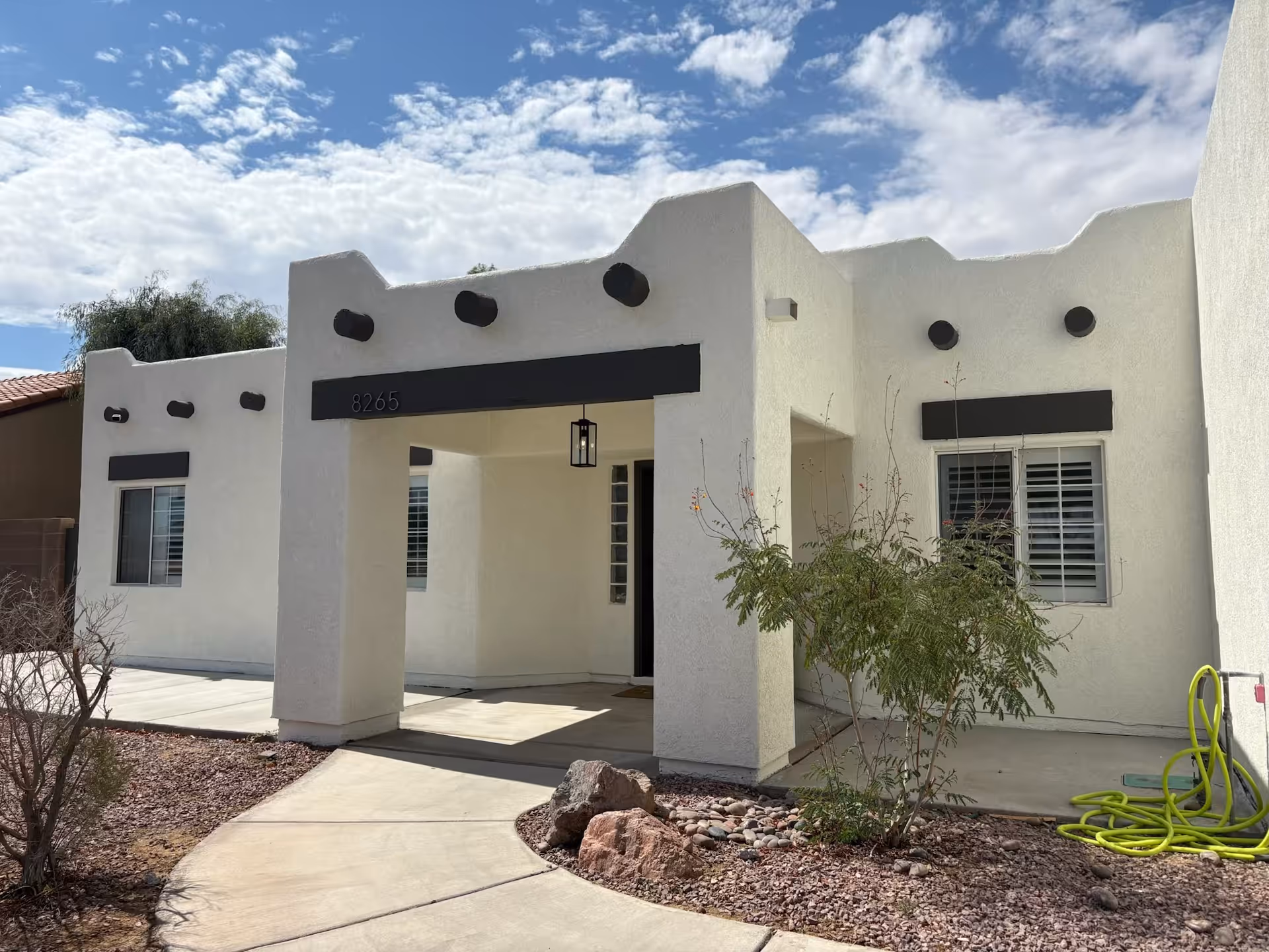 White modern building facade with a covered entrance and desert landscaping.