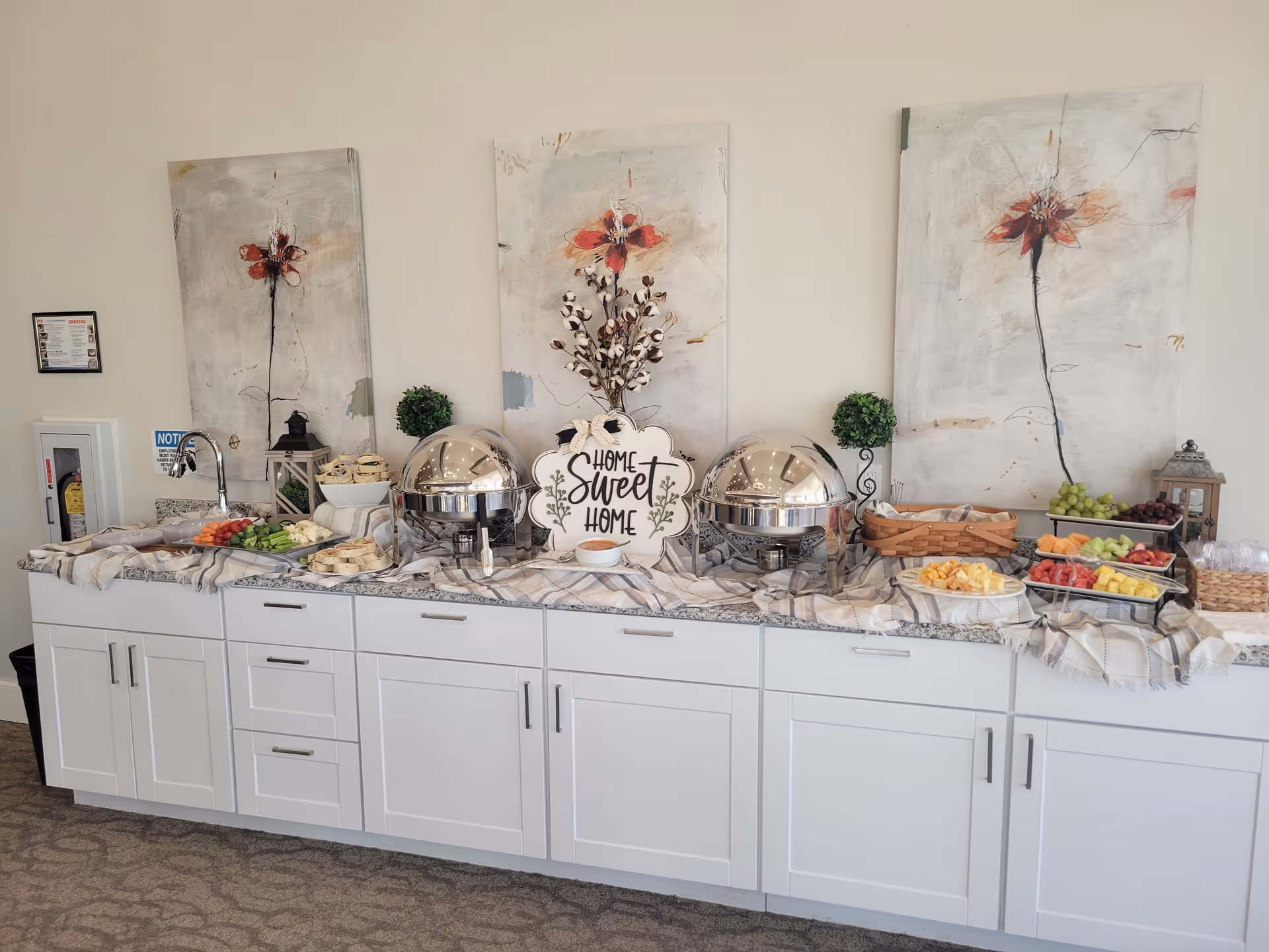 Long buffet counter with chafing dishes, fruit trays, and decorative wall art.