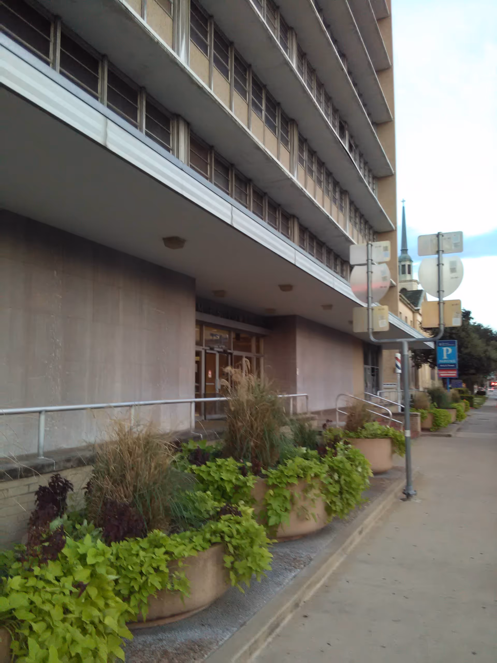 Exterior view of a multi-story senior living building with entrance and planters along sidewalk