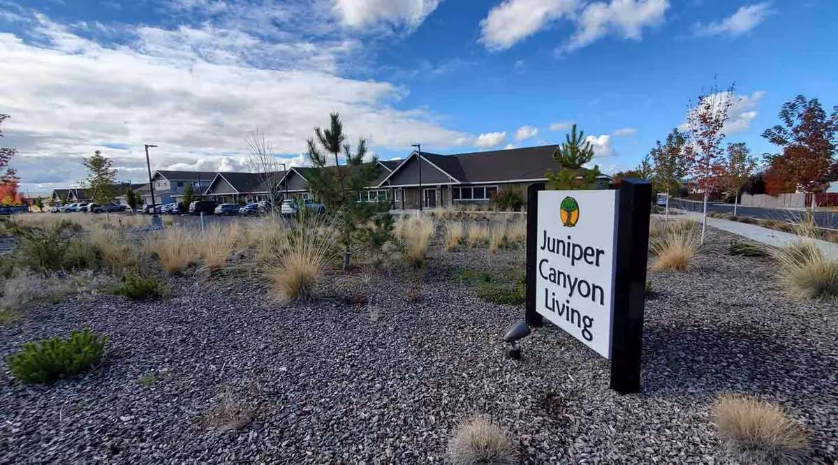 Exterior view of Juniper Canyon Living, featuring the front sign, rocky landscaping, and low lying buildings.