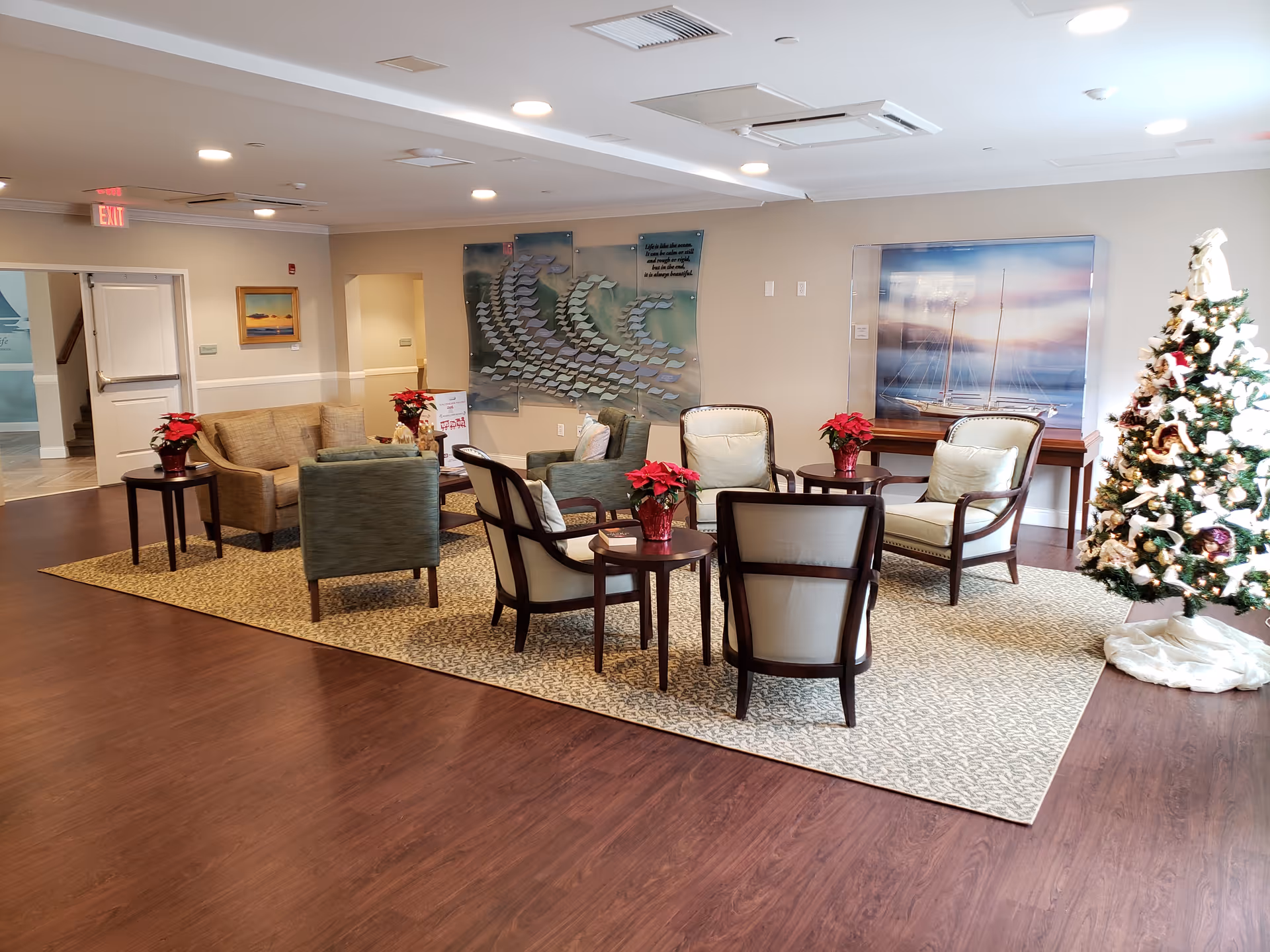 Indoor senior living lounge with couches, chairs, tables, Christmas tree, and wall art.