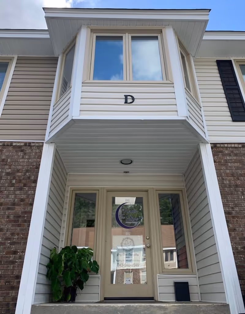Exterior view of a senior facility entrance with glass door and a balcony above.
