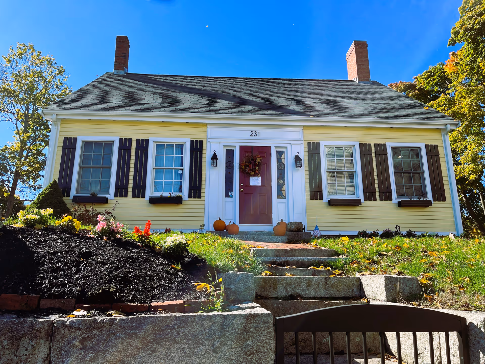 Front view of a yellow, house-style senior living building with front door and steps.