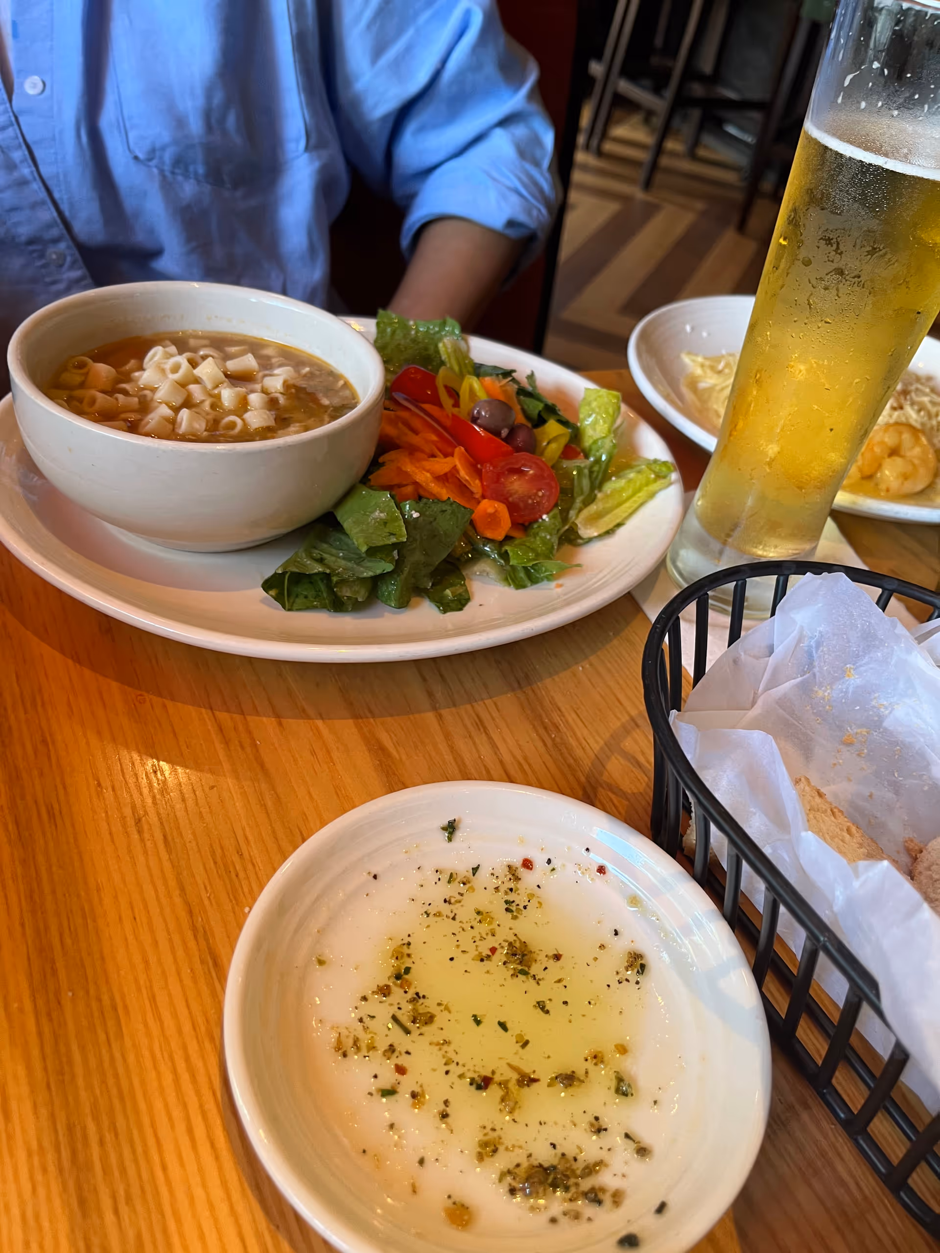 Dining table with soup, salad, bread basket, and a tall glass of beer.