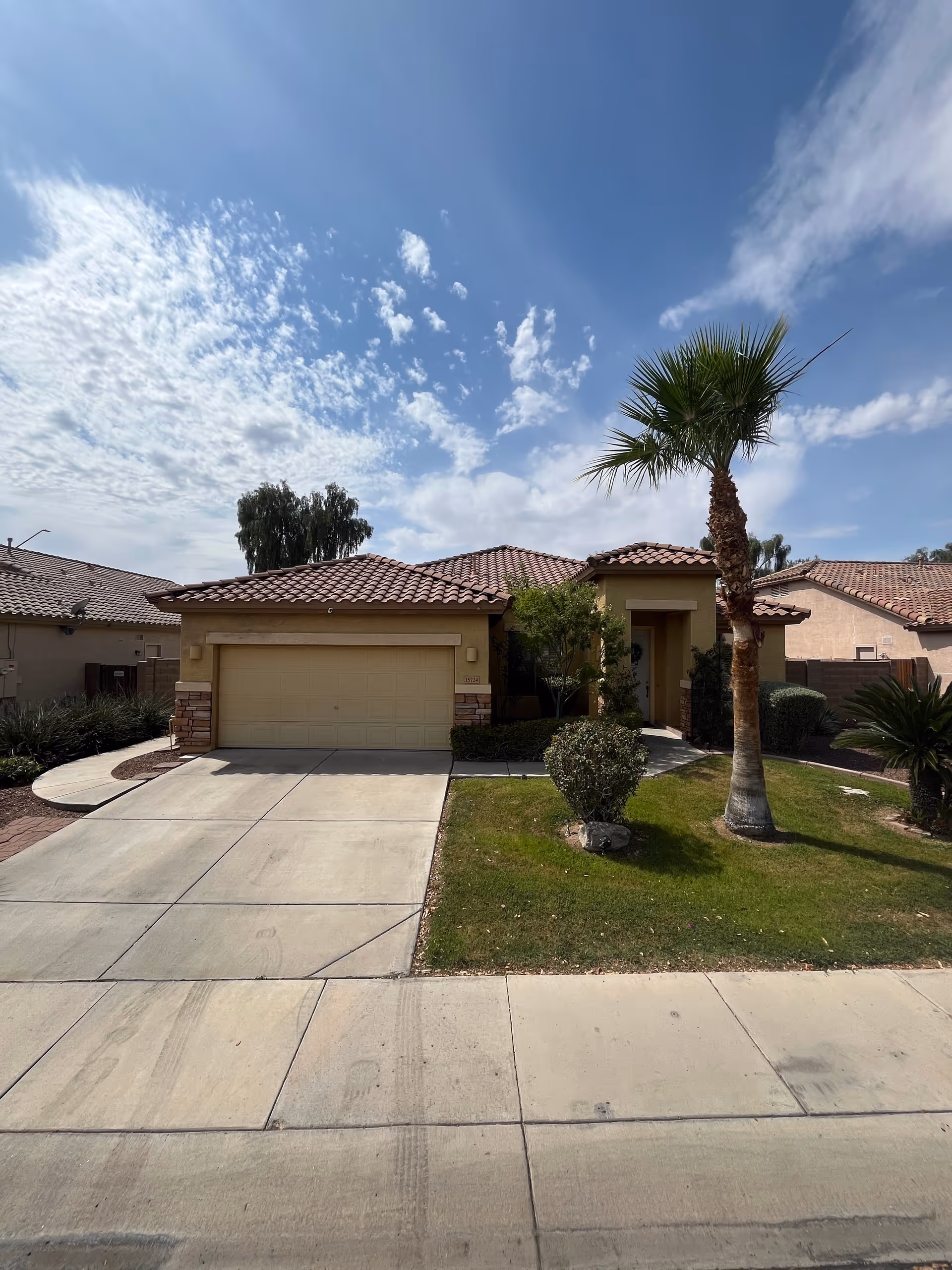 Front view of a tan, tile-roofed house with a manicured lawn and palm tree.