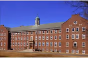 Red brick nursing building with a central entrance and cupola under a blue sky.