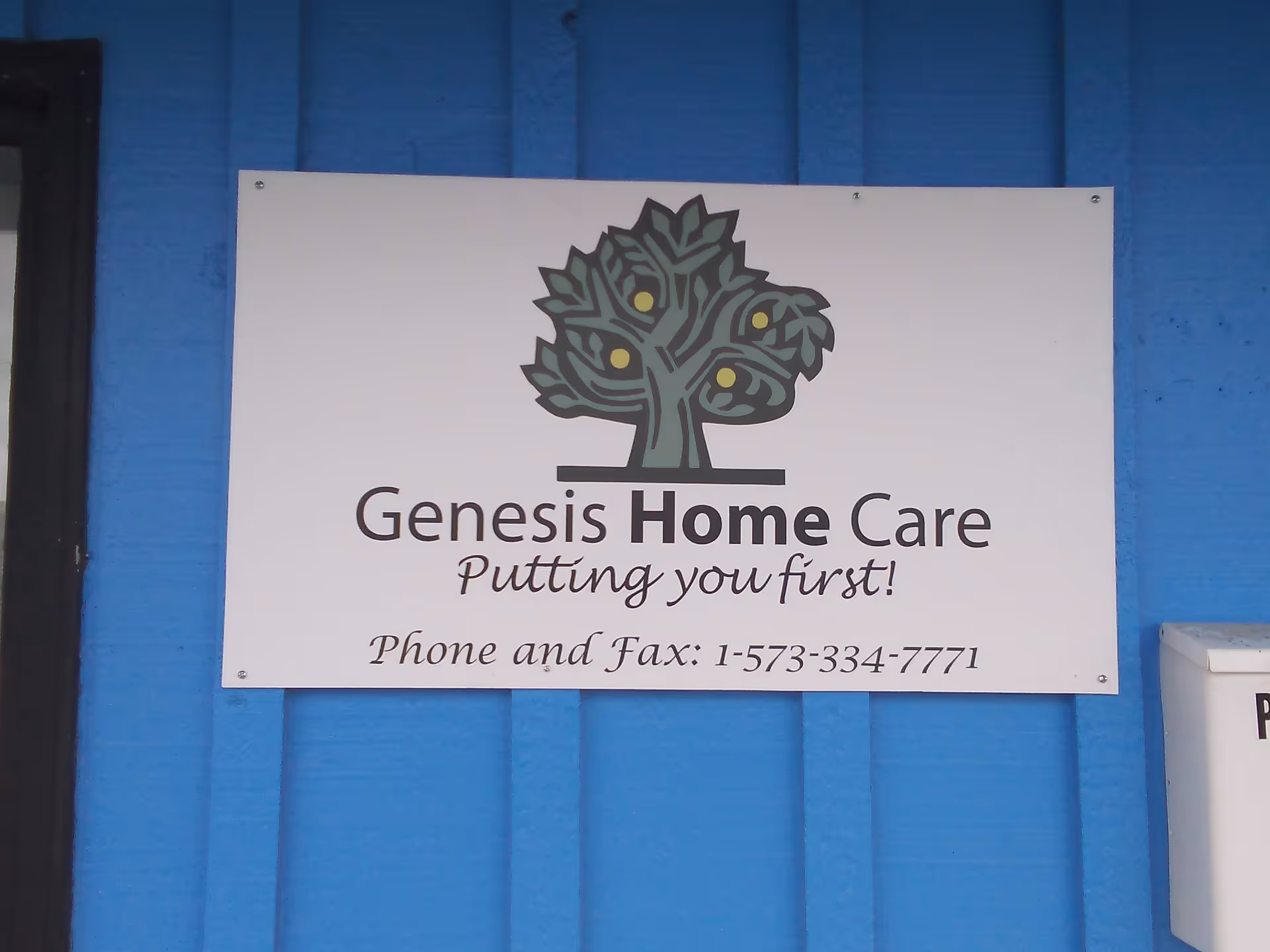 White Genesis Home Care sign with a stylized tree logo on a blue exterior wall.