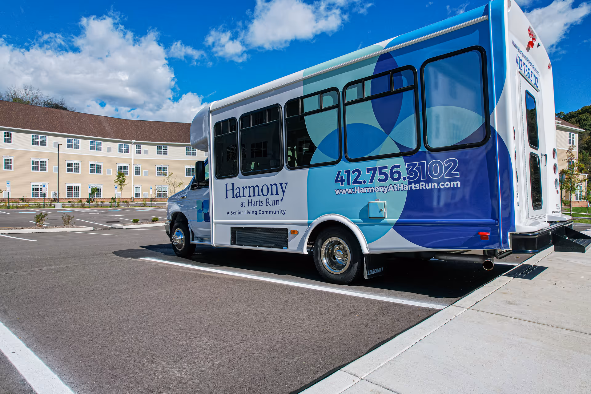Harmony at Harts Run bus parked in a lot beside a beige multi-unit building.